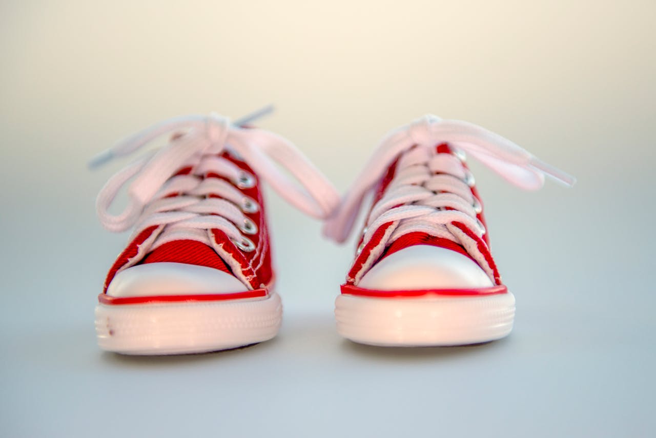 services-05 Close-up of bright red baby sneakers with white laces on a neutral background.